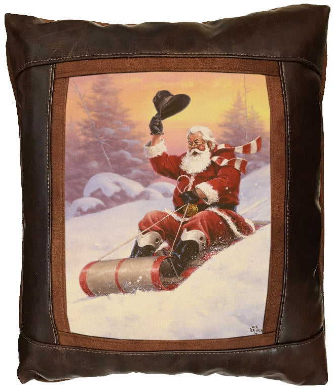 Decorative pillow with a festive design of Santa Claus holding his cowboy hat in the air while sledding down a snowy mountain with brown leather border