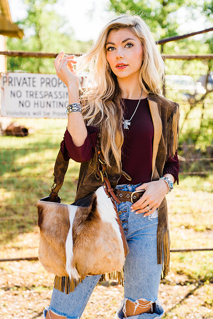 Woman holding a antelope hide bag in a rural setting with a 'Private Property' sign in the background.