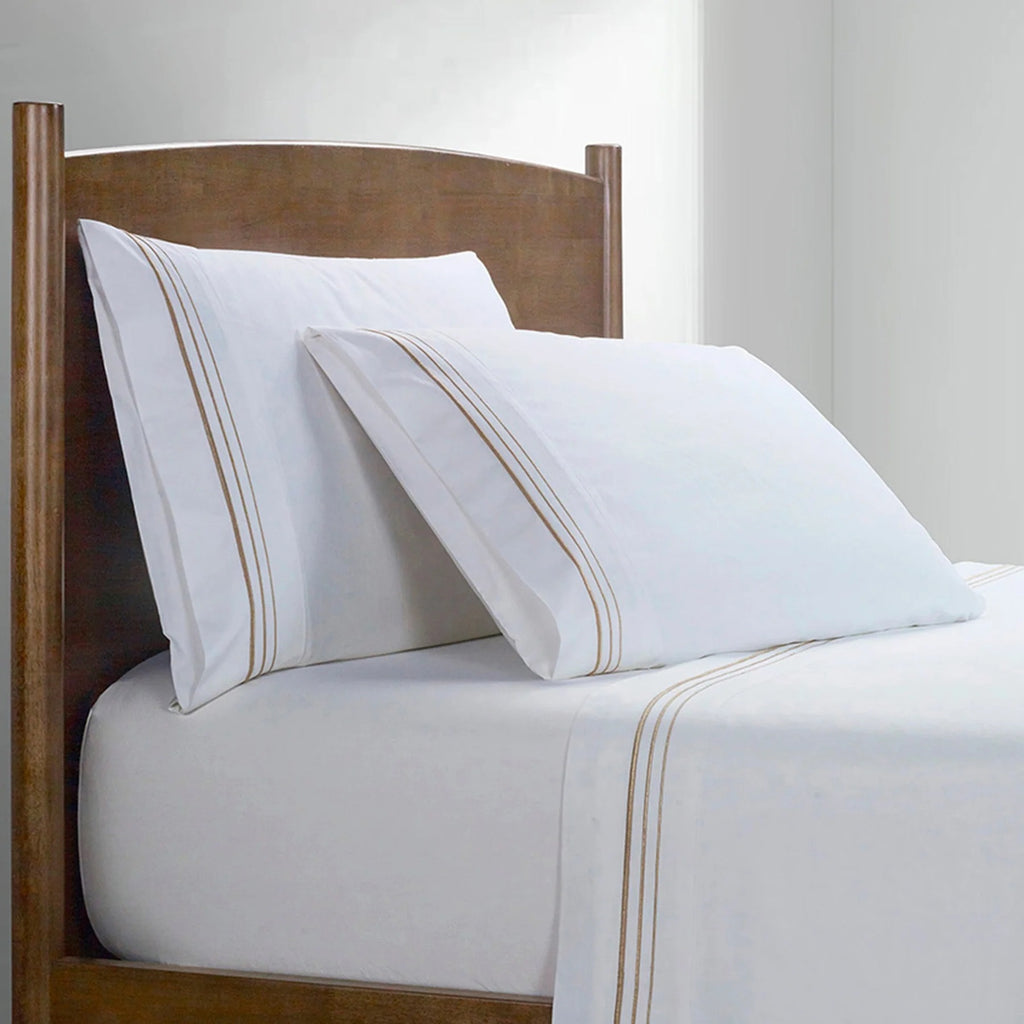 White bed sheets with gold stripes on a wooden bed frame.