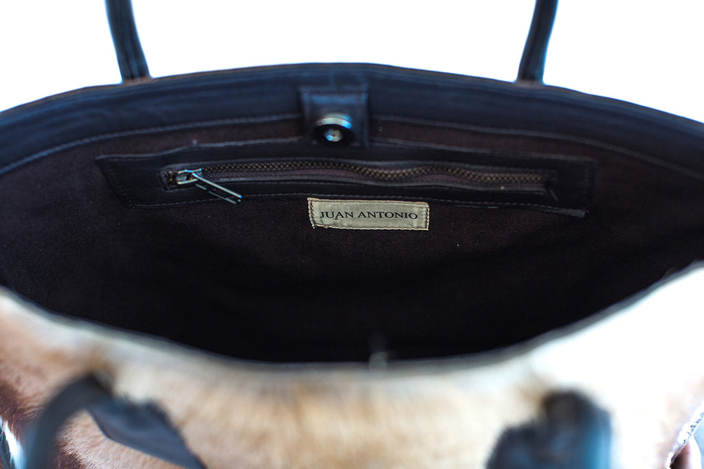 Close-up of a black handbag with 'Juan Antonio' label on a blurred background
