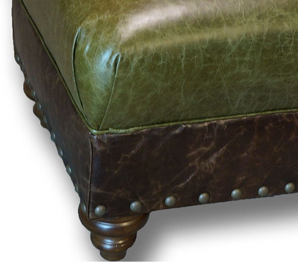 Close-up of a green leather ottoman with brown accents and nailhead trim.