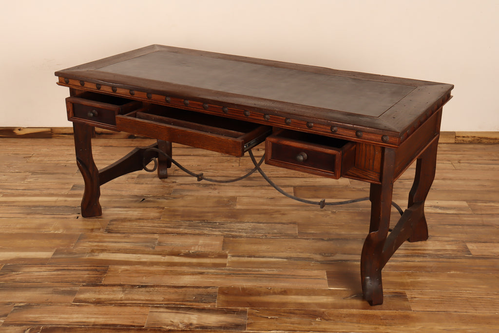 Wooden desk with leather surface on a wooden floor with drawers open.