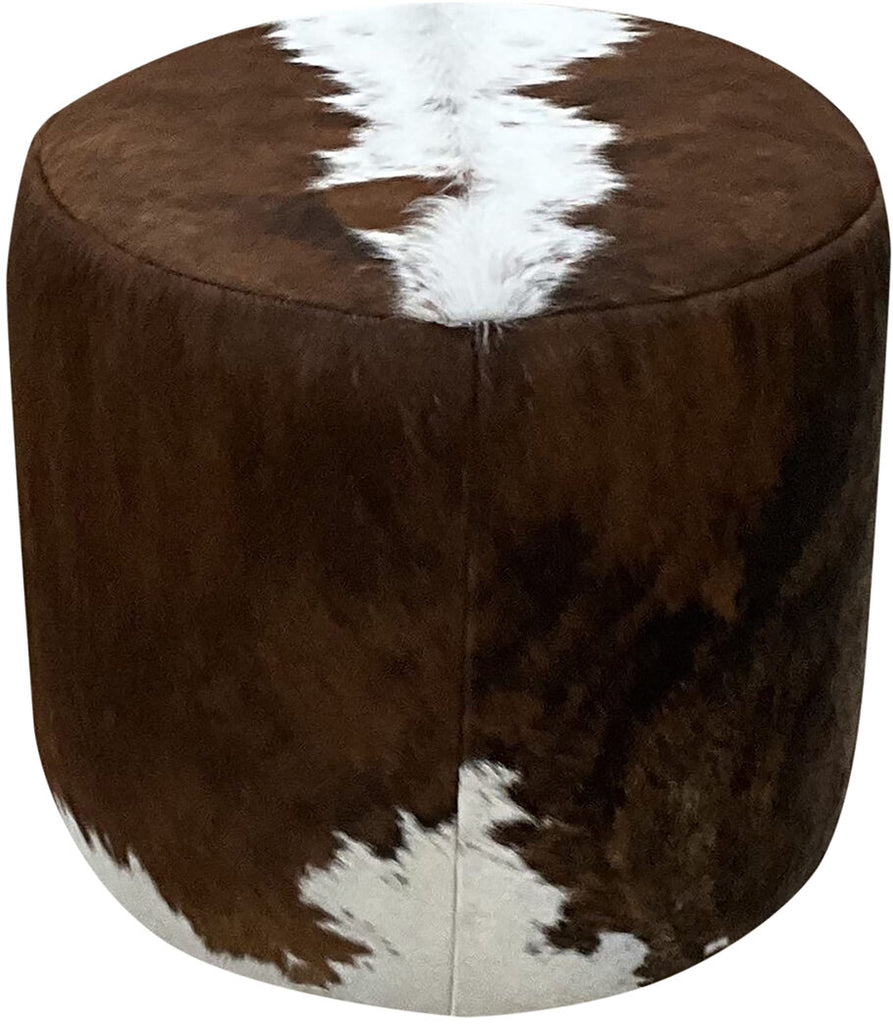 A close-up view of the Amber Round Cowhide Ottoman, showcasing its dark exotic cowhide upholstery with a striking white brindle pattern running across the top and sides.