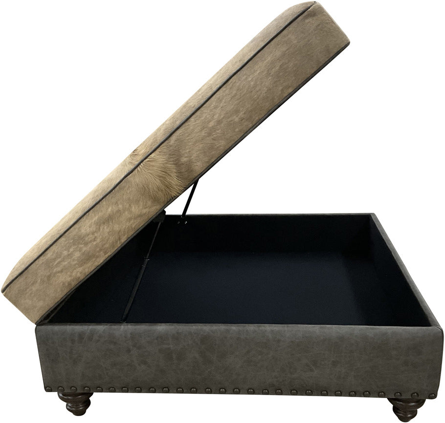 A side view of the 48" x 48" storage ottoman featuring a brindle cowhide band, Palio Grey leather lower section, and antique silver nailhead trim for a sophisticated finish.