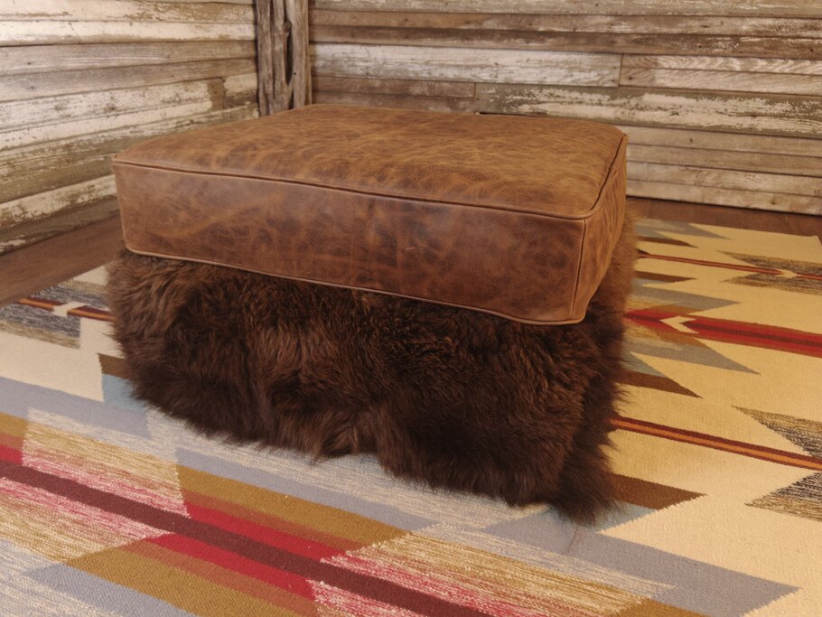 The Buffalo Ottoman (30" x 24"), featuring genuine Buffalo hide on the bottom rail and a Cora Pecan top grain leather cushion, perfect for rustic cabins and ski lodges.
