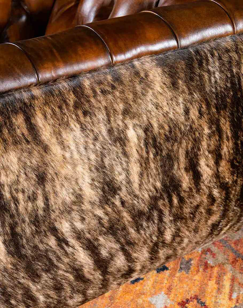 Close-up view of the Bullet Club Chair's brindle cowhide back panel, showcasing the rich texture and natural patterns paired with hand-burnished leather accents.