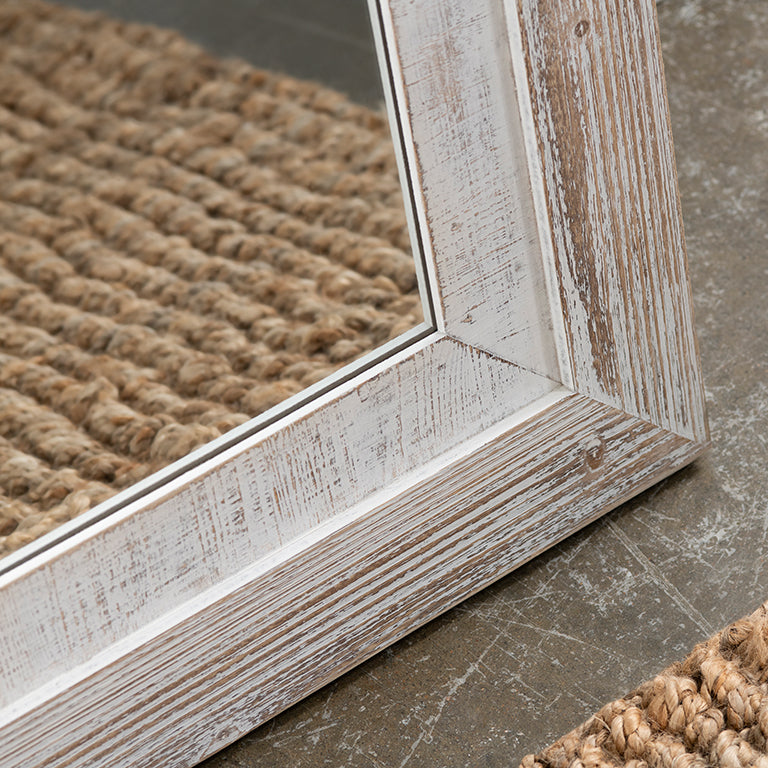 Close-up of a wooden-framed mirror with textured surface on a stone floor.