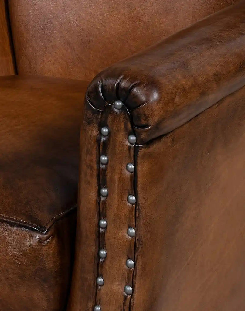 Close-up of a brown leather armchair with decorative nailhead trim.
