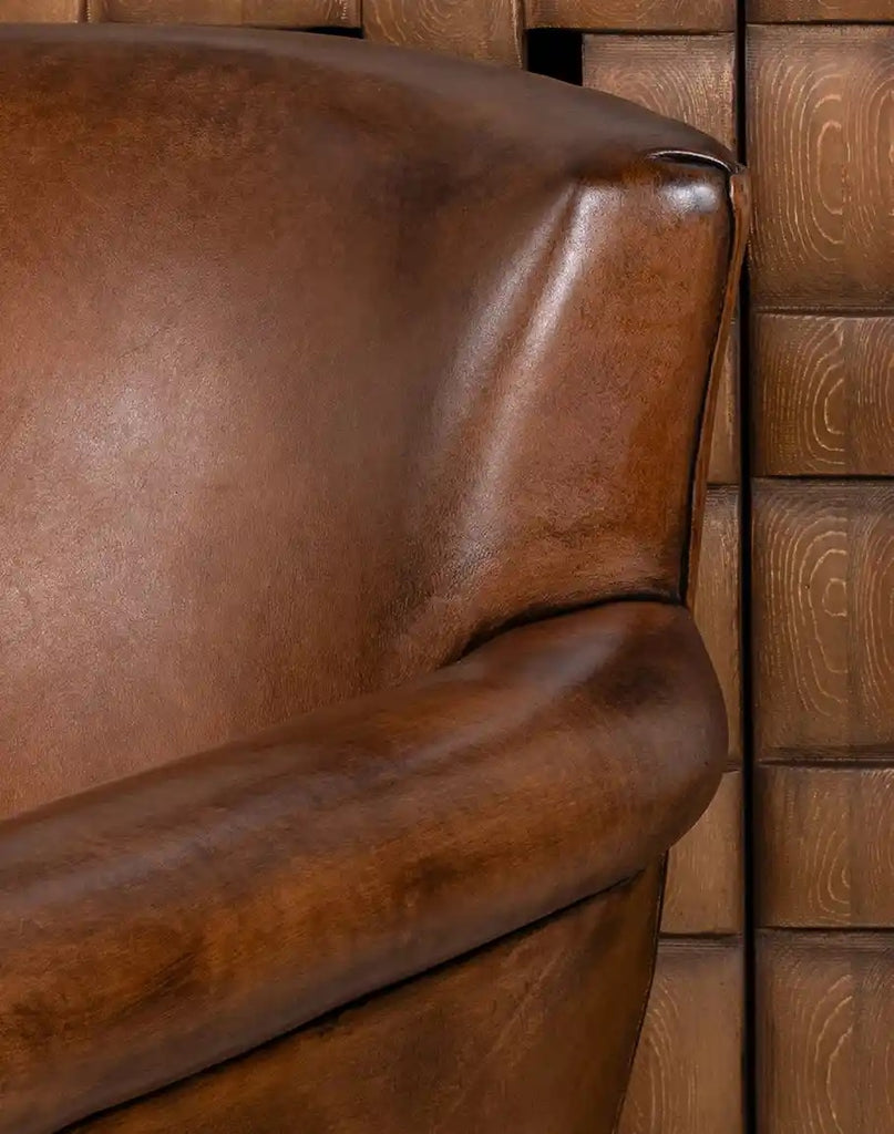 Close-up of a brown leather chair against a wooden paneled wall.