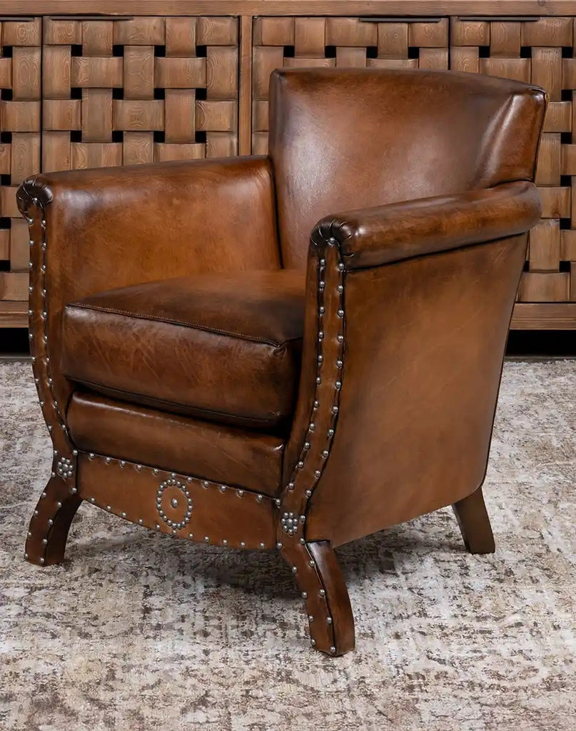 Brown leather armchair with nailhead trim against a woven wooden panel background