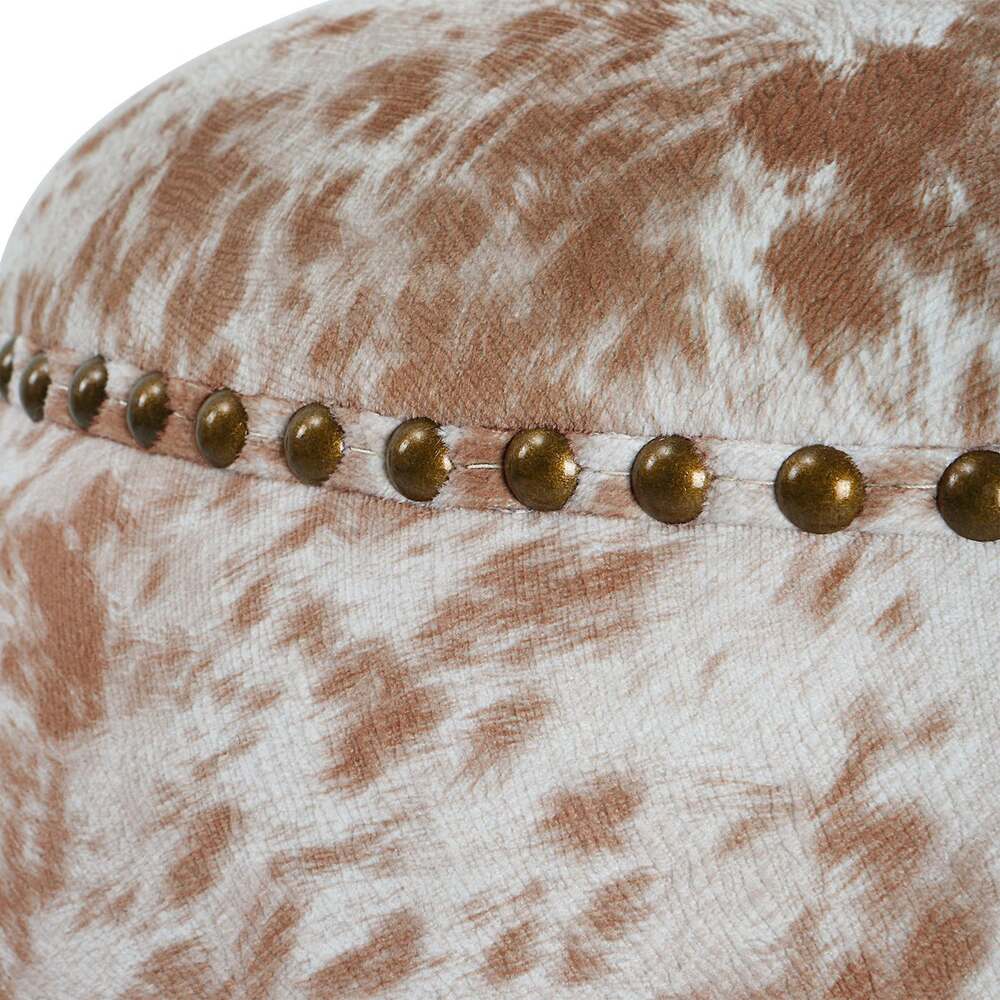 Side view of faux cowhide ottoman showcasing its antique brass nailhead detailing.