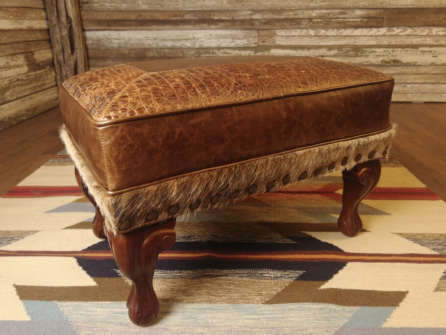 Angled view of the Giovanni Small Ottoman, showcasing its rich leather upholstery, intricate detailing, and sturdy wooden legs.