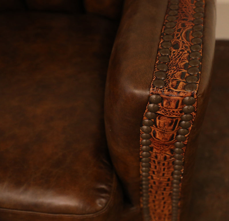 Close-up of an arm rest with embossed butternut leather with decorative nailhead trim.