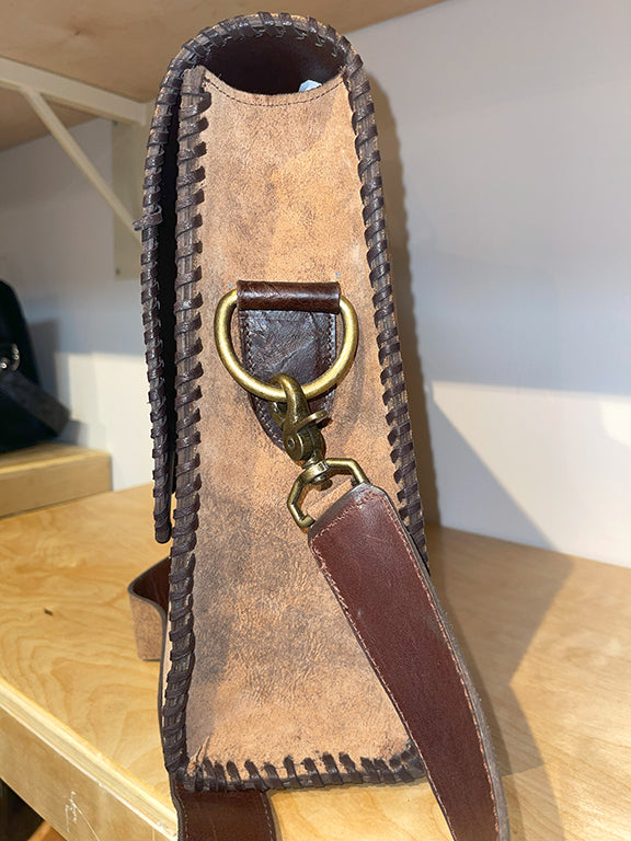 Side view of brown leather suitcase shower leather strap attached to gold ring on a wooden surface.