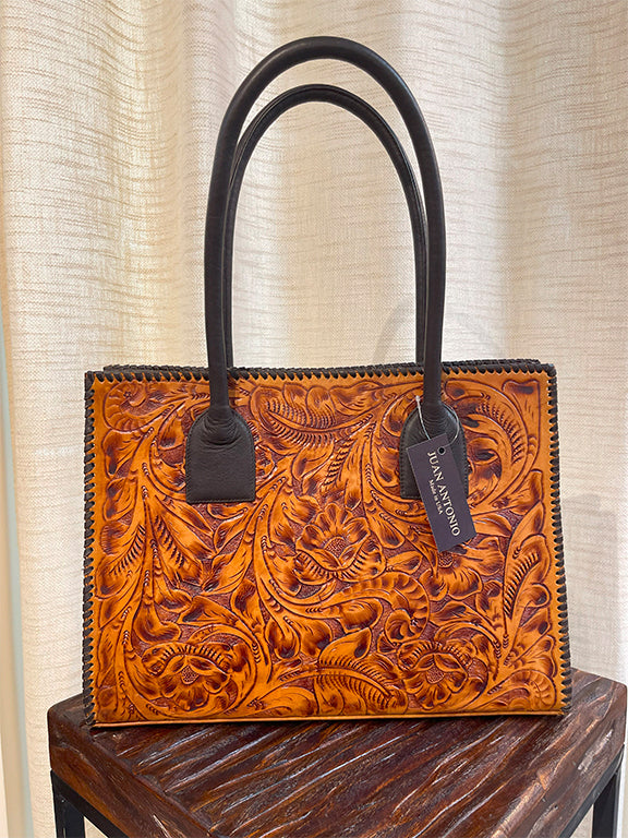 Brown leather handbag with floral embossed leather in brown with dark accents on a wooden surface