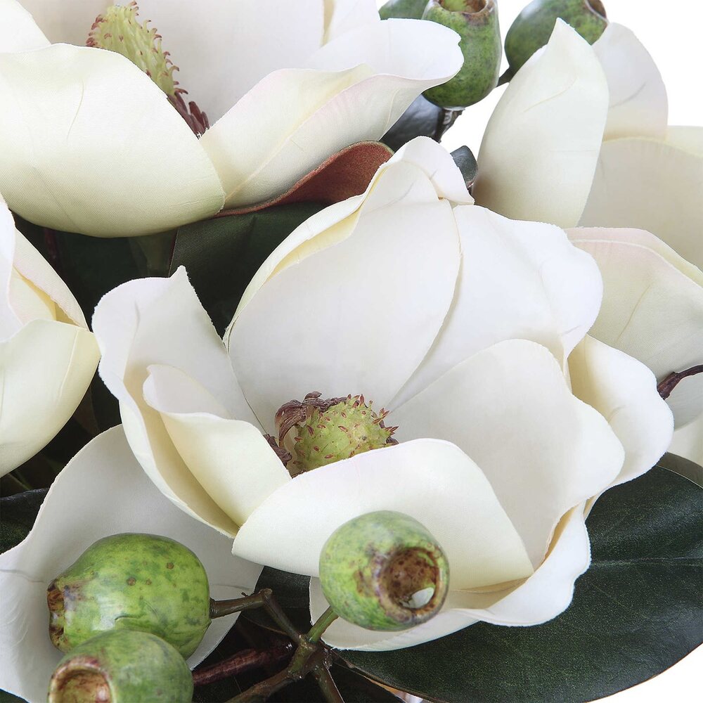 A sophisticated white magnolia bouquet in a square glass vase with faux water, accented by seed pods and natural river stones.