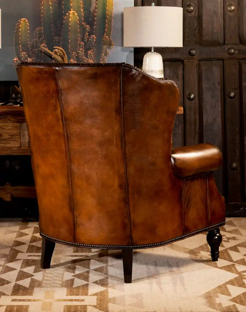 Back view of the Montana Leather Chair, showcasing its hand-burnished full grain leather, elegant curved frame, and antique brass nailhead trim in a warm Western-inspired living space.