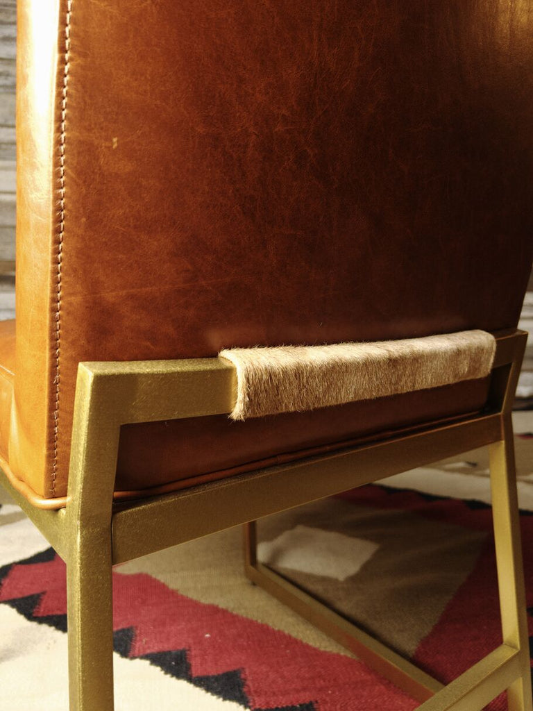 Close-up back view of the Napa Valley Dining Chair, featuring rich Mont Blanc Caramel leather upholstery, a sleek brass metal frame, and a cowhide accent detail for a refined Western touch.
