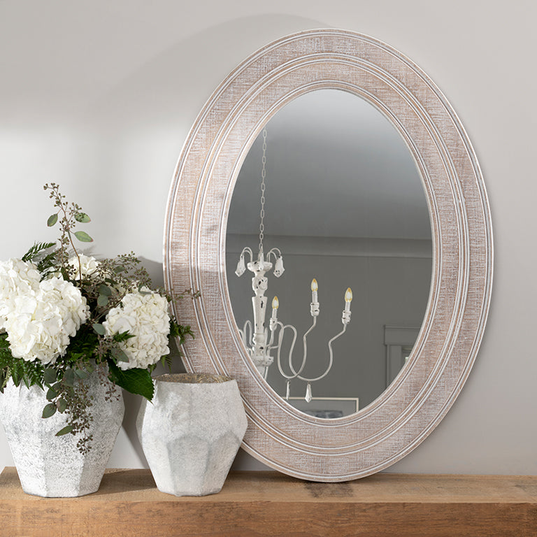 Round mirror with decorative frame on a wooden surface with flowers and vases.