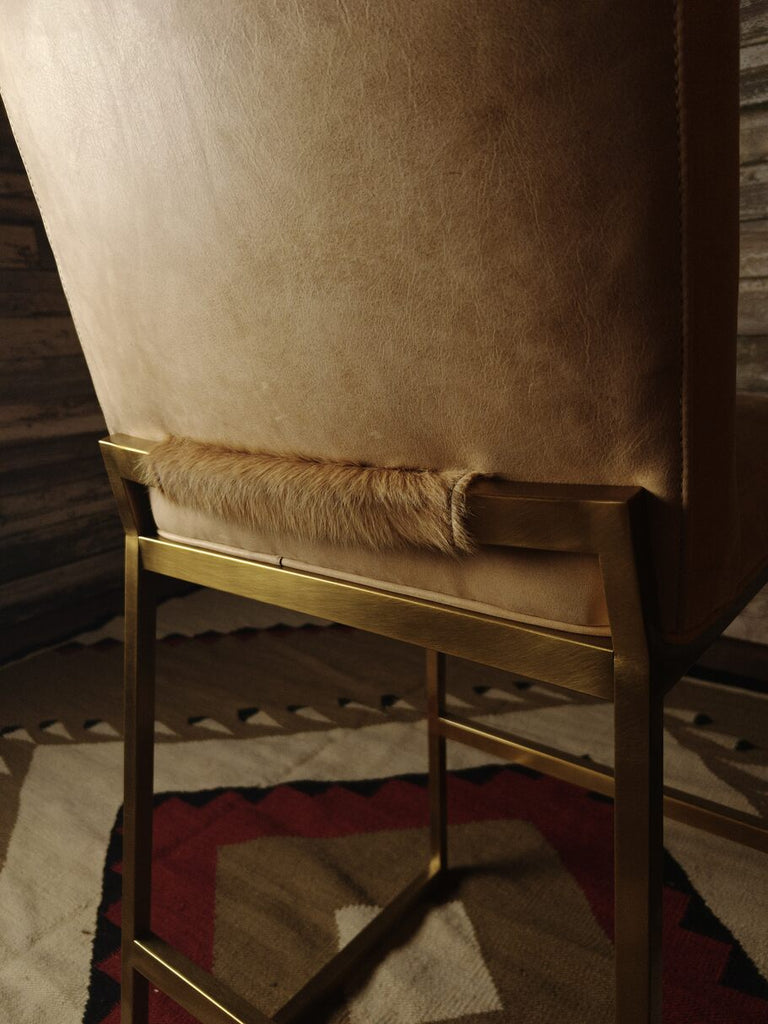 Close-up back view of the Roaring Fork Valley Barstool, featuring smooth Burnham Sunset leather, a brass metal frame, and a unique cowhide accent along the lower backrest. The image highlights the luxurious textures and Western-inspired craftsmanship.