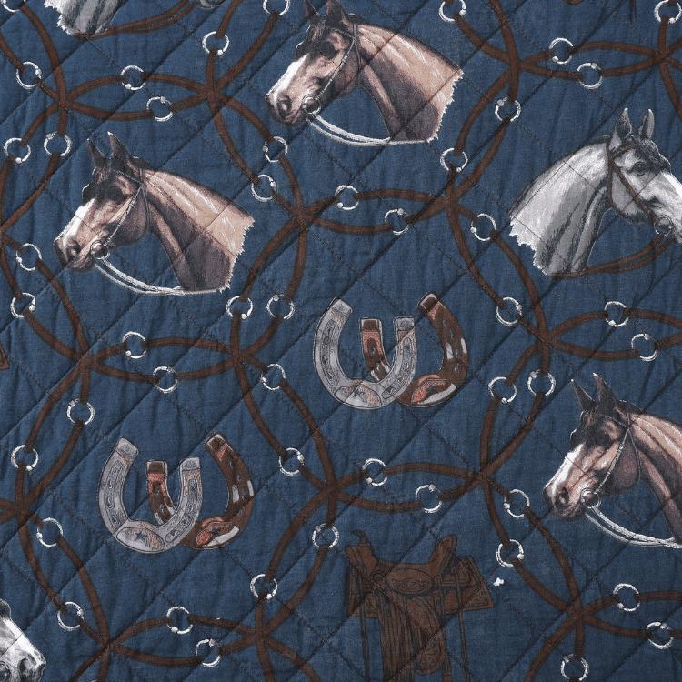 Close-up of the quilt highlighting the detailed equine illustrations surrounded by bridles and bits on the navy blue fabric.