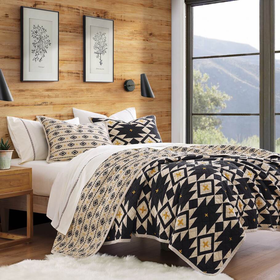 Sonoran Desert Reversible Quilt Set styled in a cabin bedroom with wooden accents, emphasizing its Southwestern charm.