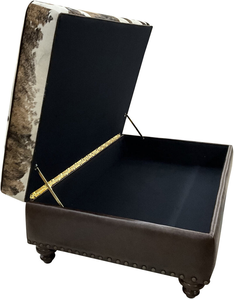 The Highlands Storage Ottoman with its cushioned top lifted, revealing a spacious black-lined storage compartment. The ottoman features a tri-color brindle cowhide top, dark brown leather sides, brass hinges, and decorative nailhead trim.