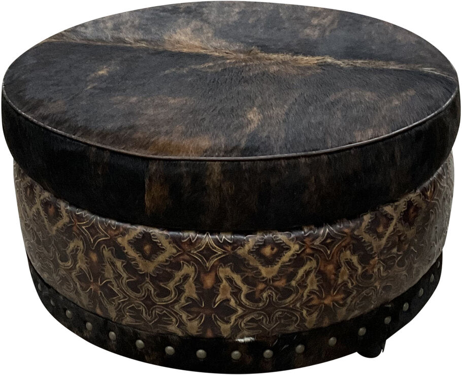 A detailed view of the River Round Storage Ottoman’s distressed dark nailhead trim, adding a refined rustic touch to its luxurious leather and cowhide design.