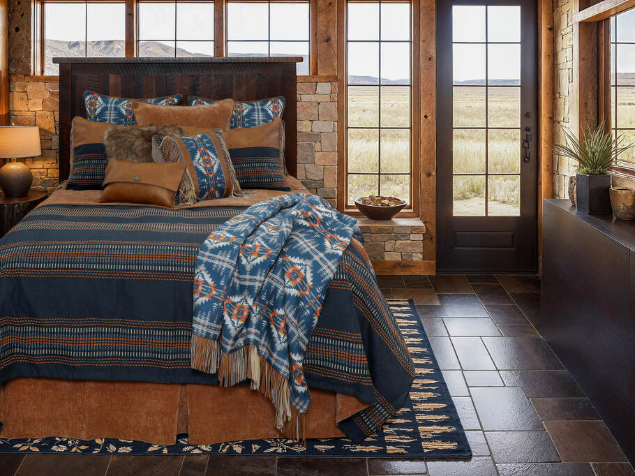 Wooded River Moreno Midnight Value Bedding Set featuring rich indigo and midnight blue tones, genuine leather accents, fringe detailing, and a relaxed turned-down coverlet panel in a navy, tan, and cream color scheme.