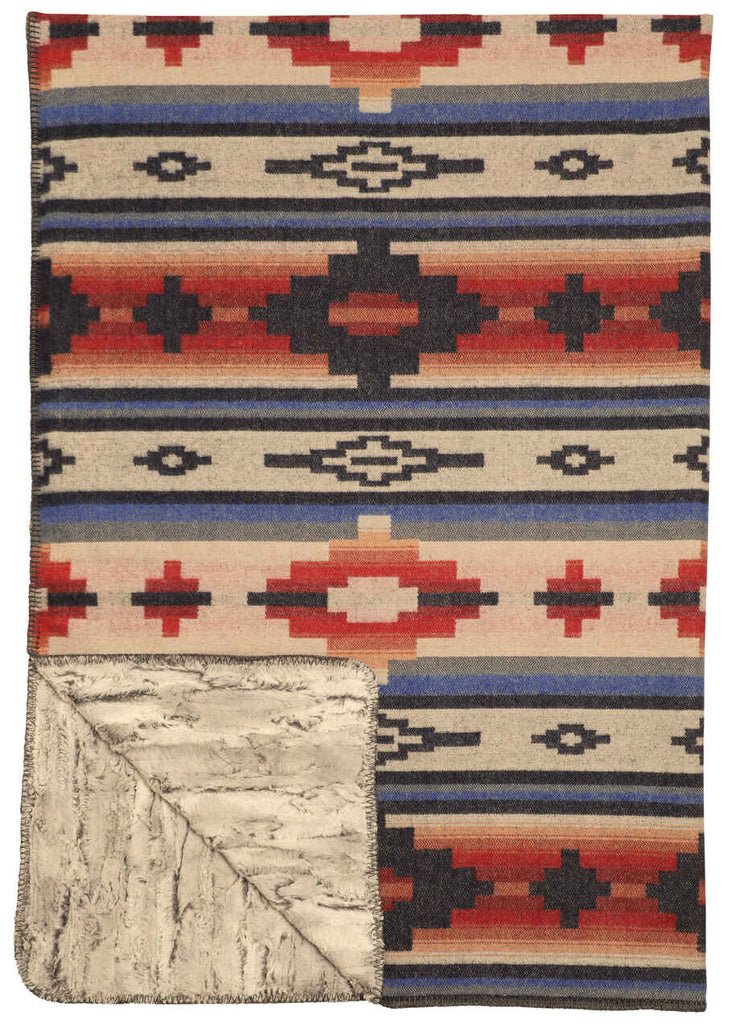 Redrock Canyon Premier Throw featuring traditional Southwestern patterns in blue, red, orange, and yellow on one side, with a soft Shadow Fox cuddle fur backing, draped over a sofa for a warm and stylish look.