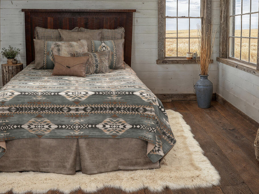 Wooded River Spearhead Dusk Value Bedding Set featuring a steely blue polyester chenille bed cover with southwestern diamond patterns, faux leather panels, authentic leather fringe accents, and coordinating pillow and euro shams; displayed in a rustic bedroom setting for a refined, adventurous look.